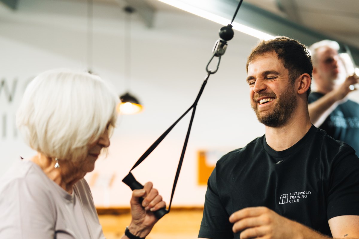 A coach working with a member on the cable machine, both laughing